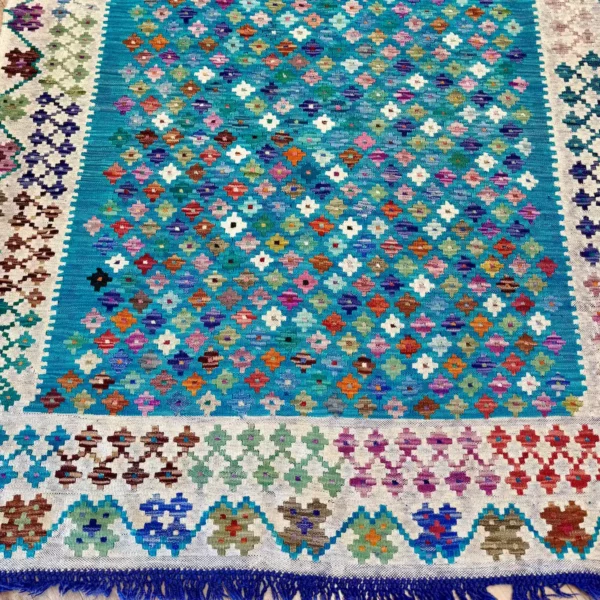 Kilim fait main aux motifs géométriques multicolores après nettoyage, fond bleu turquoise ravivé