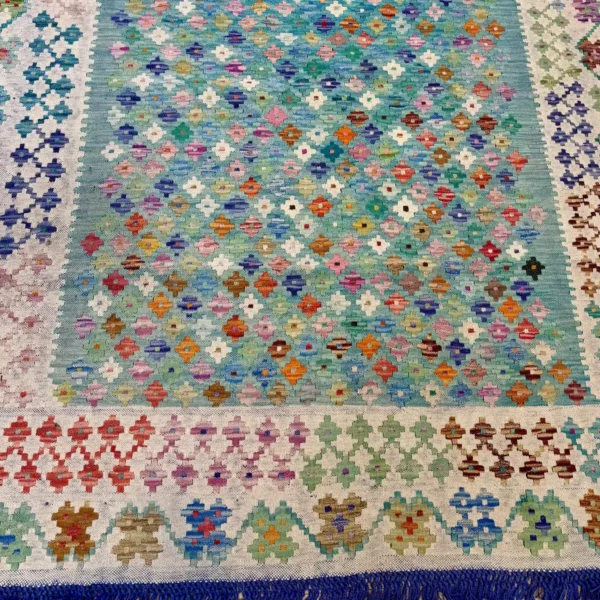 Kilim fait main aux motifs géométriques multicolores avant nettoyage, fond beige légèrement terni