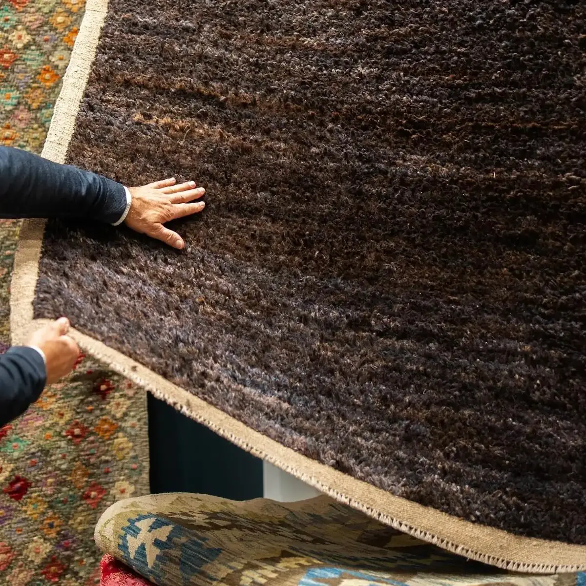 Expert services Galerie Simon inspectant la texture d'un tapis ancien brun lors d'une expertise